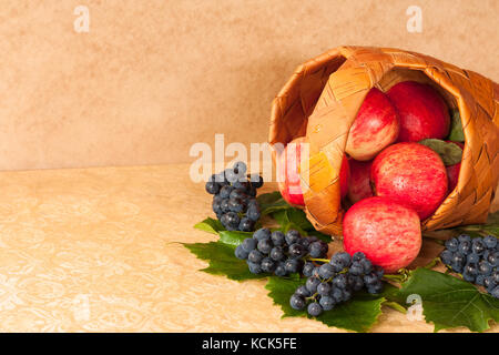 Cibo sano. mele rosse nel cesto di vimini e uva con foglie sul tavolo. close up e copyspace. Foto Stock