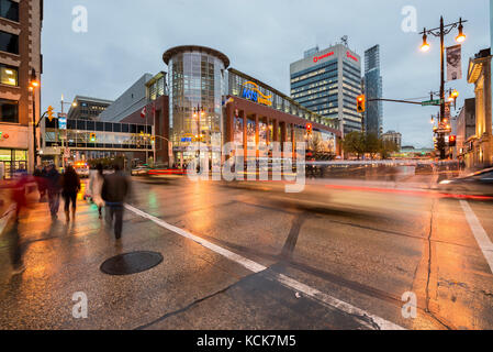 Le persone che attraversano le Portage Avenue nella parte anteriore del Centro MTS al crepuscolo downtown Winnipeg in Manitoba, Canada Foto Stock