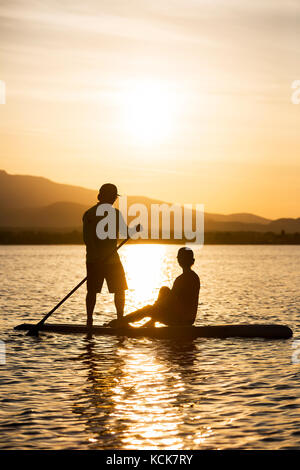 Una giovane coppia in silhouette, pagaia una tavola in piedi su come la sera si mette mentre alla fine del parco regionale di Goose Spit a Comox. La Comox Valley, Vancouver Island, British Columbia, Canada. Foto Stock