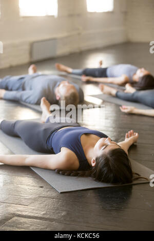 Un gruppo di giovani sportivi a praticare yoga lezione con istruttore in palestra, giacenti nel corpo morto esercizio, facendo, savasana cadavere pongono gli studenti relaxina Foto Stock