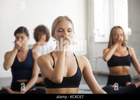 Un gruppo di giovani sportivi a praticare yoga lezione con istruttore, rendendo narice alternativo di respirazione, nadi shodhana pranayama esercizi, in seduta Foto Stock