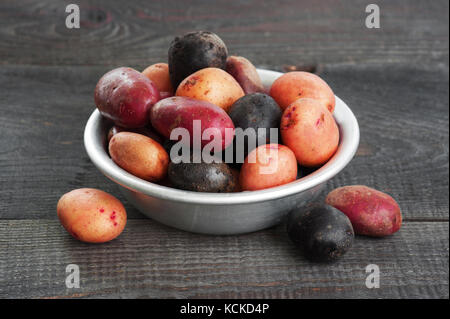 Freschi patate colorate nel recipiente di metallo sul vecchio tavolo in legno Foto Stock