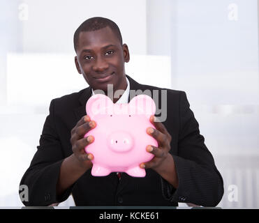 Ritratto di un giovane africano imprenditore tenendo piggybank Foto Stock