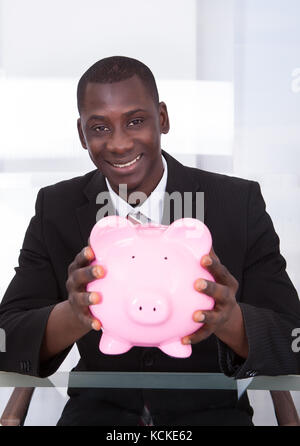 Ritratto di un giovane africano imprenditore tenendo piggybank Foto Stock