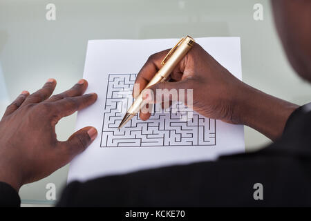 Close-up di un imprenditore guardando maze puzzle tenendo pen Foto Stock