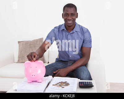 Felice l'uomo africano seduto sul divano con documento e piggybank Foto Stock