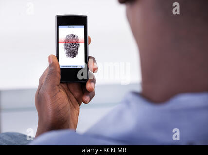 Persona in possesso di telefono cellulare che mostra l'applicazione con il processo di scansione di impronta digitale su una schermata Foto Stock