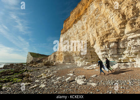 Surfers camminare sotto le scogliere a seaford head sulla costa di East Sussex, Inghilterra. South Downs national park. Foto Stock