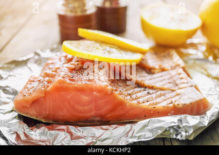 Big Pink pezzo di salmone con erbe e limone si appoggia su un lucido pezzo di carta stagnola. Foto Stock
