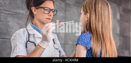 Pediatra femmina usando un bastoncino di cotone per prelevare un campione da un paziente la gola Foto Stock