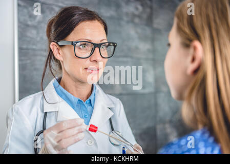 Pediatra femmina usando un bastoncino di cotone per prelevare un campione da un paziente la gola Foto Stock