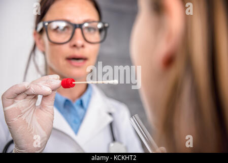 Pediatra femmina usando un bastoncino di cotone per prelevare un campione da un paziente la gola Foto Stock