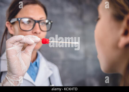 Pediatra femmina usando un bastoncino di cotone per prelevare un campione da un paziente la gola Foto Stock