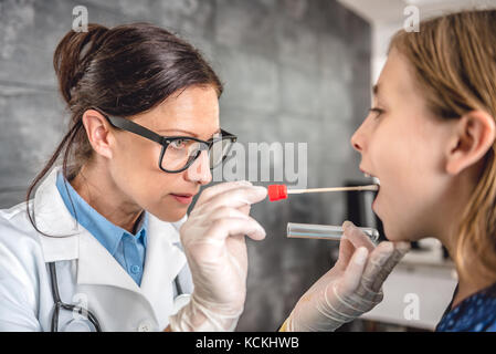 Pediatra femmina usando un bastoncino di cotone per prelevare un campione da un paziente la gola Foto Stock