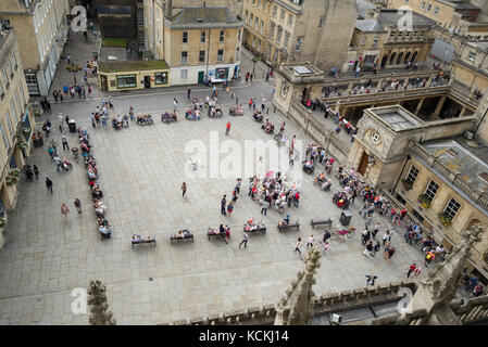 Vista aerea di turisti seduti sui banchi e in gruppi guardando e ascoltando il violoncellista in Kingston Parade, con bagni romani adiacenti, Bath, Regno Unito Foto Stock