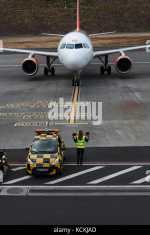 Aeromobile marshaller a Cristiano Ronaldo Aeroporto Internazionale guide un Easyjet Airbius A319 al suo supporto di stazionamento. Foto Stock