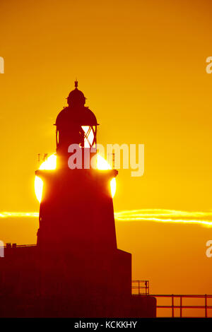 Molo Blyth e faro all'alba con sole direttamente dietro la luce Foto Stock