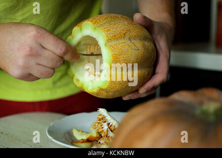 Insolito halloween melone, processo di taglio, le sementi e gli avanzi sul tavolo della cucina. Foto Stock