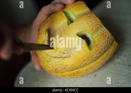 Insolito halloween melone, processo di taglio, il coltello e il maschio mani. messa a fuoco selettiva e bokeh di fondo. Foto Stock