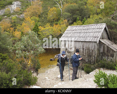 Due escursionisti che si parte dal lago Crater Boatshed circondato da faggi decidui (Fuscospora gunnii) in autunno fogliame. Cradle Mountain-Lake St Clair Foto Stock