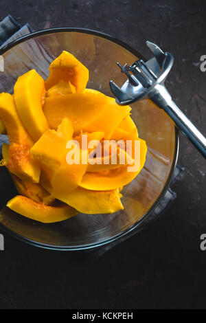 Grandi pezzi di zucca in una ciotola di vetro e frullatore close-up verticale Foto Stock