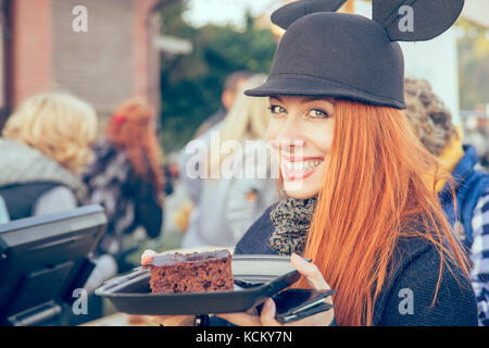 Carino donna felice in un cappello di mangiare una fetta di torta all'aperto Foto Stock