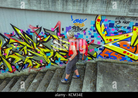 Figura femminile in rosso le passeggiate di fronte all imponente urban graffiti nel sottopasso di calcestruzzo, Austria, Stams, Austria, Foto Stock