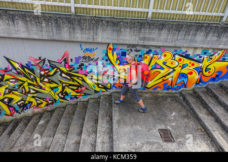 Figura femminile in rosso le passeggiate di fronte all imponente urban graffiti nel sottopasso di calcestruzzo, Austria, Stams, Austria, Foto Stock