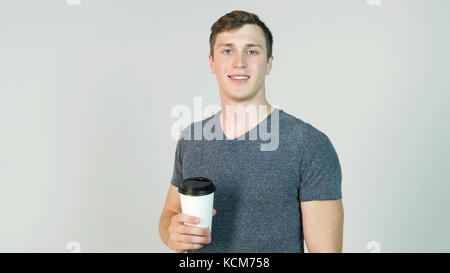 Giovane uomo di bere il caffè usa e getta dal bicchiere di carta su sfondo bianco Foto Stock