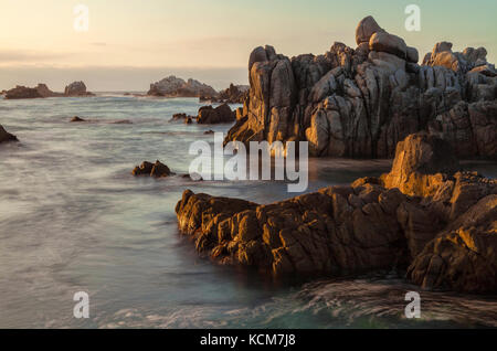 La luce del sole serale si riflette sulle rocce e sui fondali marini lungo la penisola di Monterey, California. Foto Stock