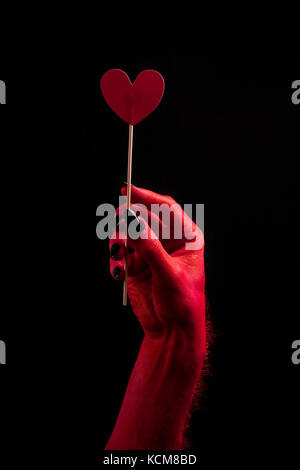 Diavolo Rosso mano che regge un cuore simbolo. concetto di halloween Foto Stock