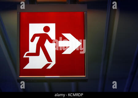L'uscita di emergenza segno mostra la direzione di fuga in caso di pericolo. l'uscita di emergenza pende scheda sul soffitto dell'edificio. Foto Stock