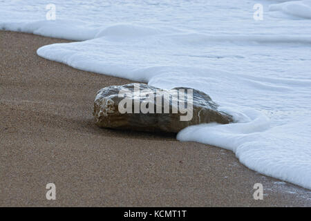 Singola pietra in surf sulla spiaggia sabbiosa, West Bay, Dorset, Regno Unito Foto Stock
