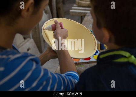 Potter femmina assistere suo figlio in pittura una ciotola al negozio di ceramiche Foto Stock