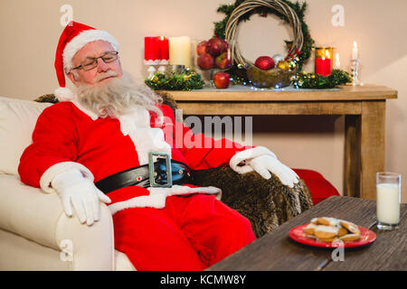 Santa Claus rilassante sul divano nel soggiorno di casa durante il periodo natalizio Foto Stock