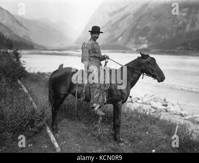 Immagine di un cowboy che cavalca un cavallo attraverso un campo, probabilmente raffigurante lo stile di vita rurale e agricolo dei primi anni del XX secolo. Foto Stock