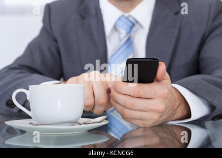 Close-up di commercianti tramite telefono cellulare con tazza di caffè posto a scrivania Foto Stock