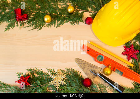 Casco di protezione, mason gli strumenti e le decorazioni di Natale su sfondo di legno Foto Stock