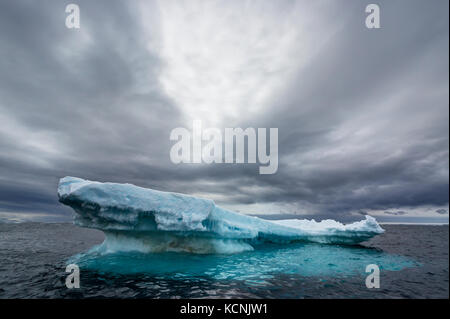 Un iceberg galleggiante lascia lentamente posto all'inevitabile assalto dell'oceano sotto un cielo drammatico vicino all'isola di Joinville, alla penisola antartica, all'Antartide Foto Stock