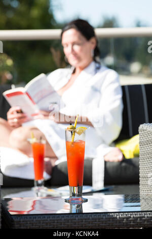 Una donna matura si rilassa nel patio esterno con un cocktail mentre si visita il Kingfisher Resort and Spa. Courtenay, Vancouver Island, British Columbia, Canada Foto Stock