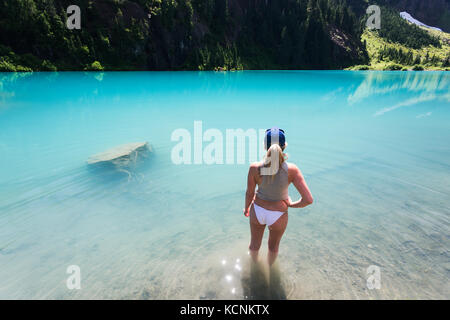 Una giovane donna si rilassa nelle acque turchesi del secolo sam lago in strathcona park, l'isola di Vancouver, British Columbia, Canada Foto Stock