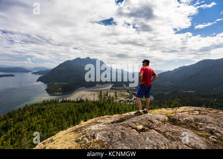 Un escursionista è ricompensato con splendide vedute della baia di Kelsey, Johnstone strait e il salmone estuario del fiume da un punto di vista di alta sopra la valle Sayward, Isola di Vancouver. Foto Stock
