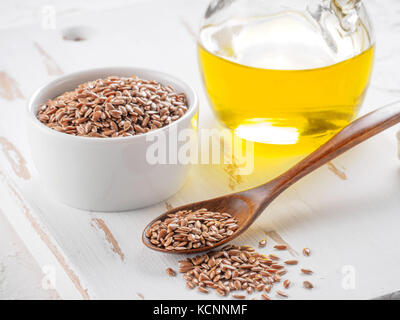 Brown semi di lino in cucchiaio e olio di lino in una bottiglia di vetro bianco su sfondo di legno. Olio di lino è ricco in acido grasso omega-3. Foto Stock