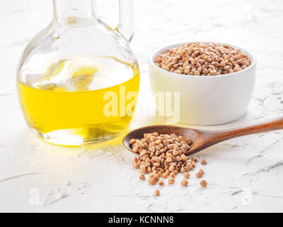 Brown del grano saraceno in cucchiaio di farina di grano saraceno e olio in bottiglia di vetro bianco su sfondo di legno. Copia dello spazio. Foto Stock