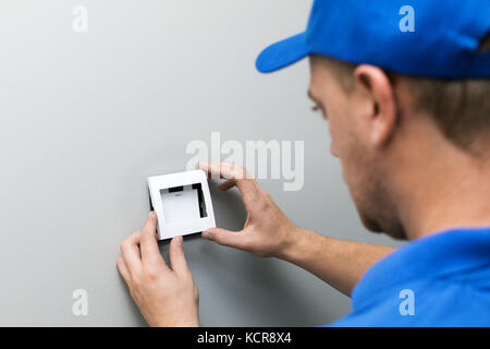 Elettricista in uniforme blu installazione interruttore di luce sulla parete Foto Stock