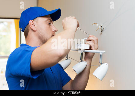 Elettricista a lavoro - installazione lampada a parete Foto Stock