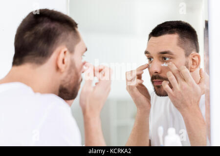 Giovane uomo di applicare la crema per il viso a bagno Foto Stock