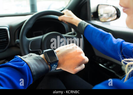 Immagine ritagliata della donna che guarda la smart watch durante la prova di guida in auto Foto Stock