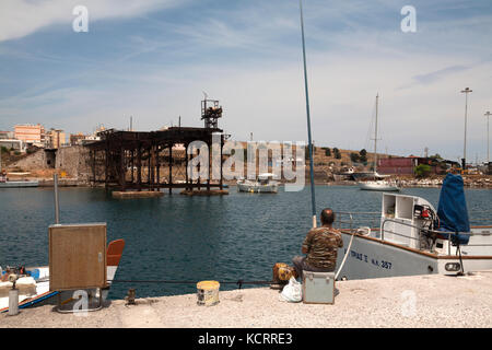 Lavrio Port Attica Grecia uomo la pesca nei pressi di ferro vecchio Quay del francese Mining Company nel 1887 ora un monumento del patrimonio industriale Foto Stock