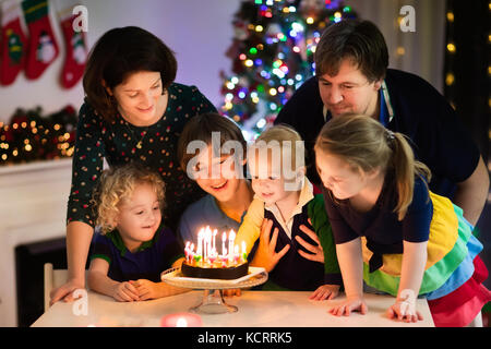 Famiglia festeggia il compleanno e il natale. bambino nato vigilia di Natale candele di soffiaggio sulla torta. padre, madre e bambini mangiare nuovo anno dessert. genitori un Foto Stock